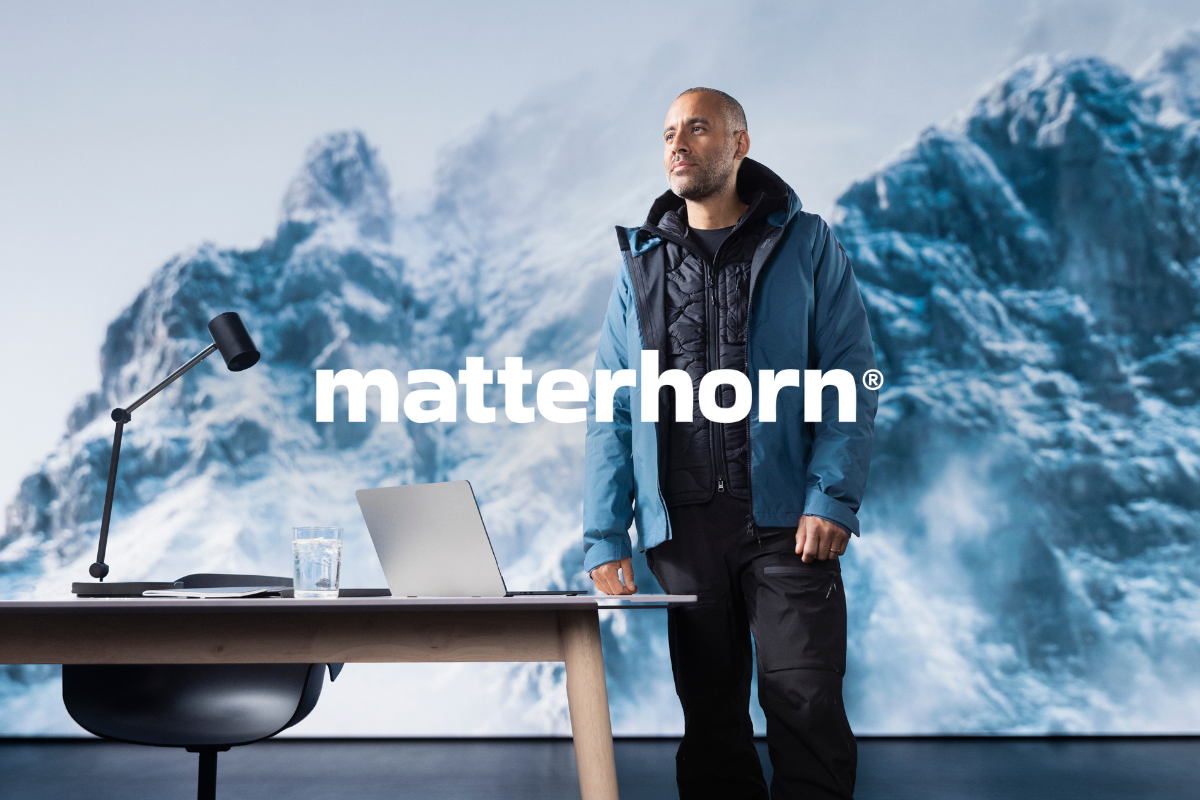 Man i funktionskläder står vid skrivbord med laptop, snötäckta berg i bakgrunden. Klickbar länk till Matterhorn-produkter